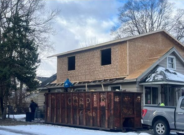 A dumpster is parked in front of a house under construction.