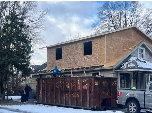 A dumpster is parked in front of a house under construction.