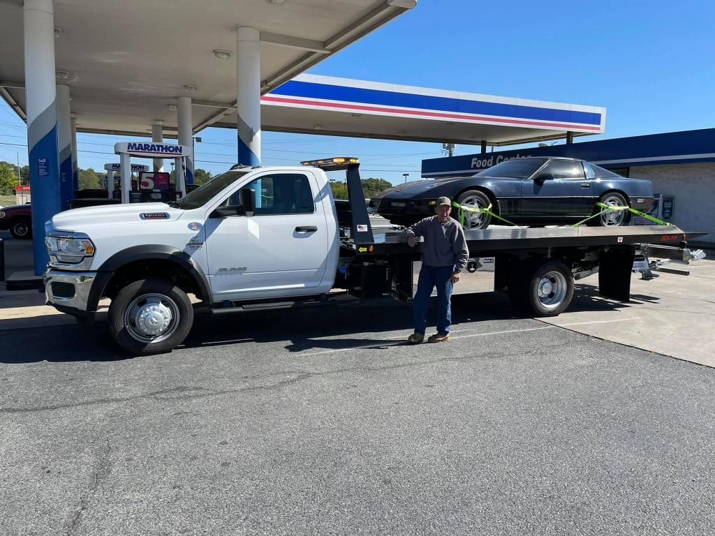 A man is standing next to a tow truck with a car on the back.