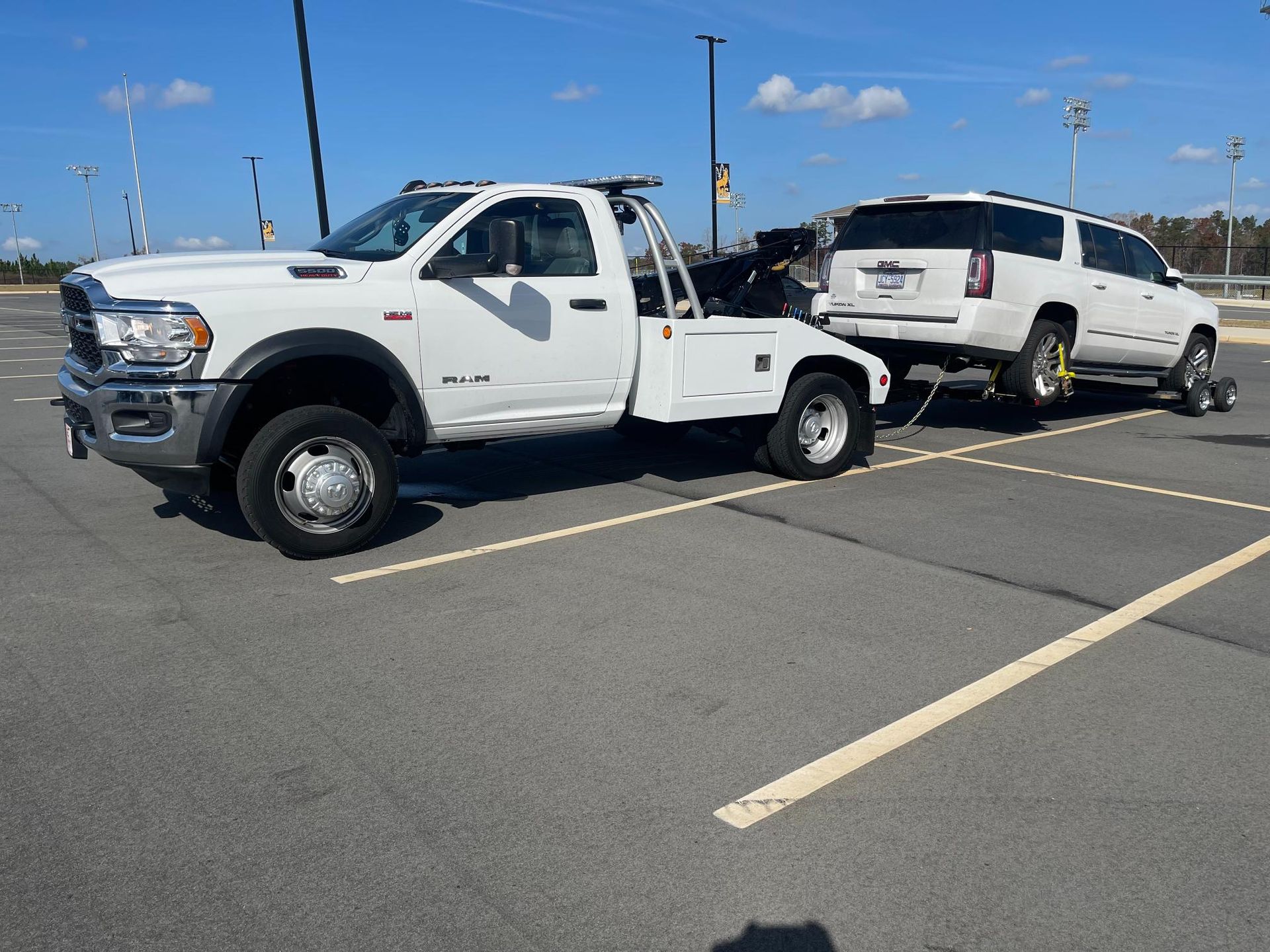A white tow truck is towing a white suv in a parking lot.