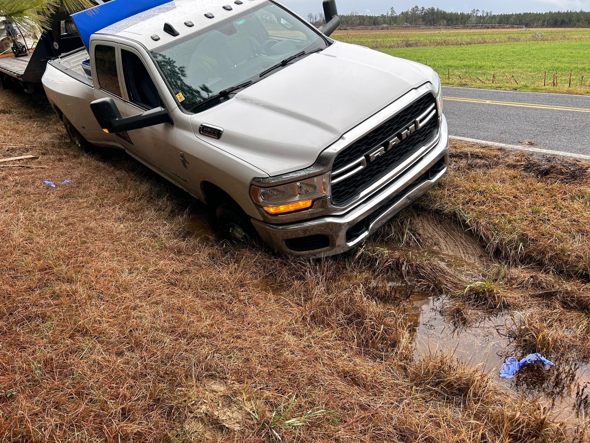 A white truck is stuck in the mud on the side of the road.
