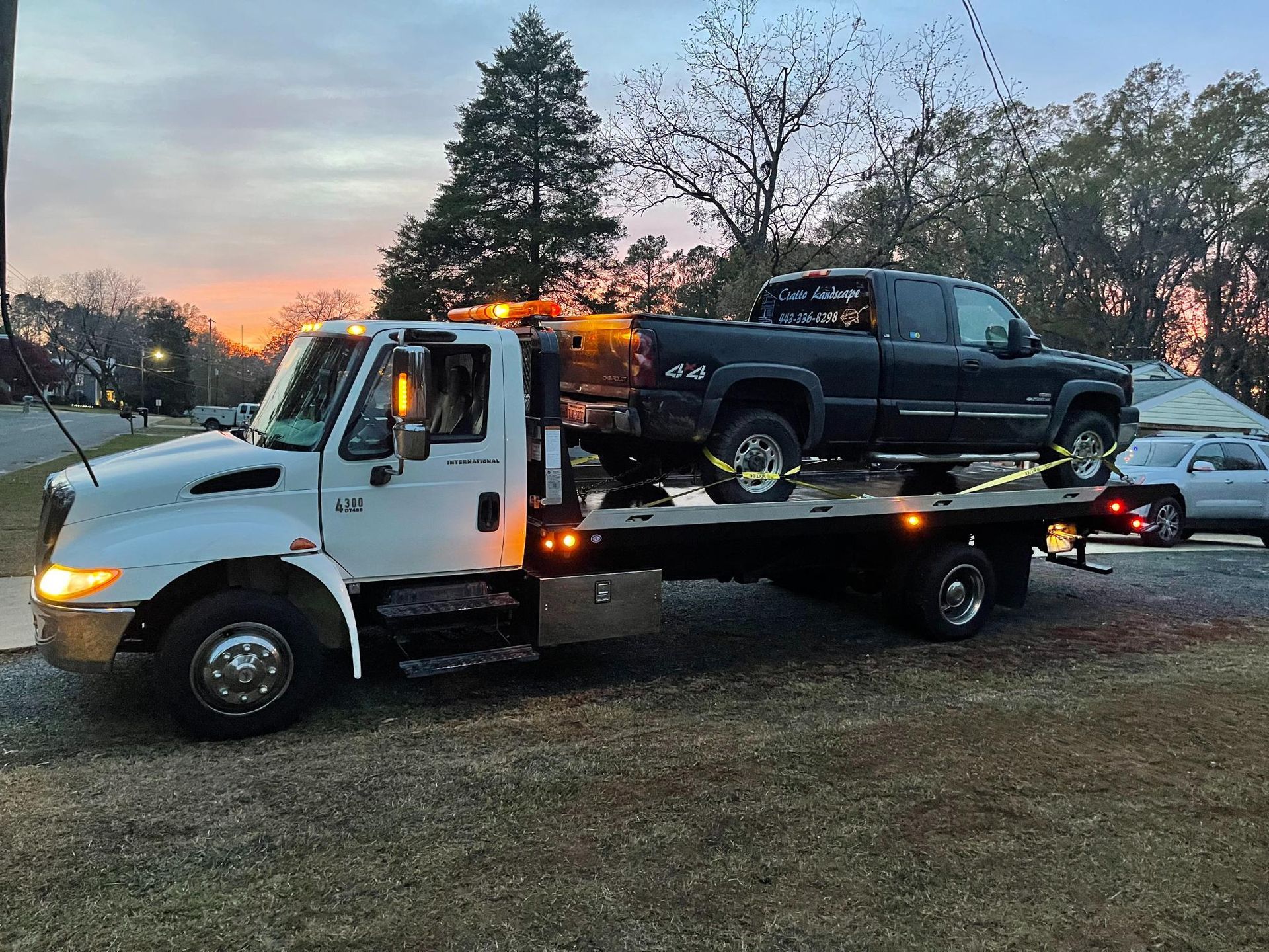A tow truck is carrying a black truck on the back of it.
