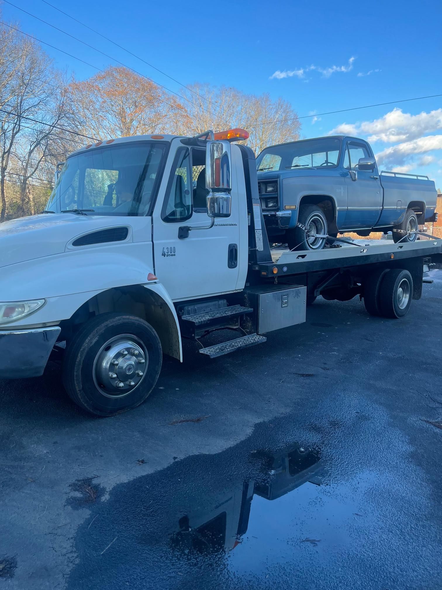 A white tow truck is towing a blue truck.