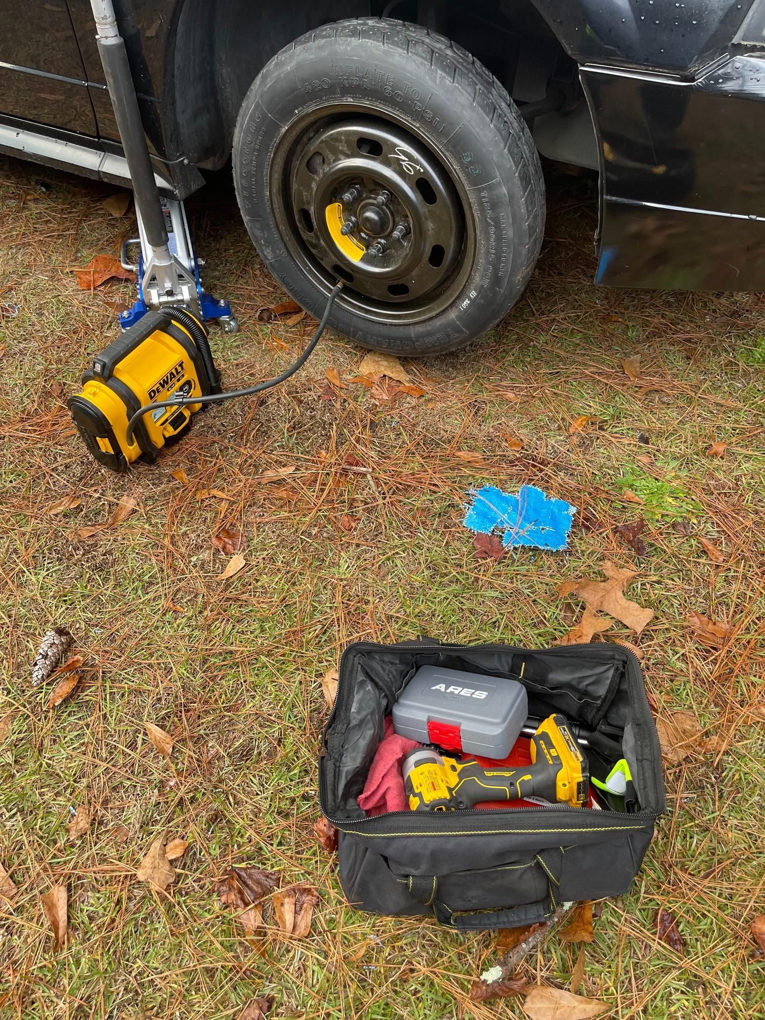 A car with a flat tire is sitting on the ground next to a tool bag.