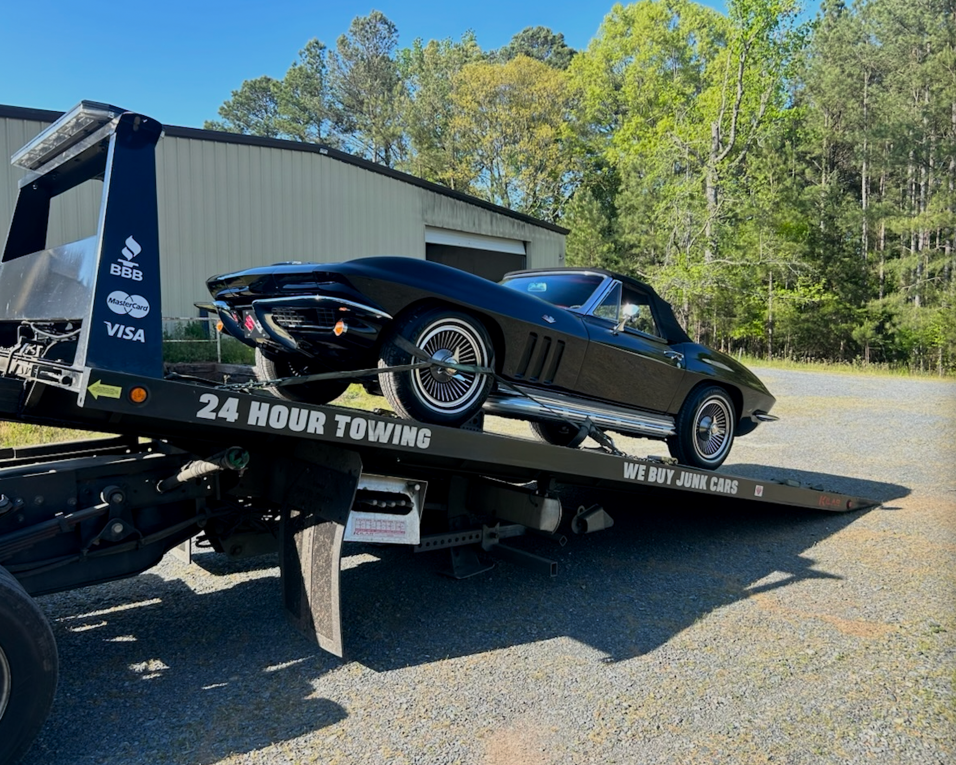 A black corvette is sitting on top of a tow truck.
