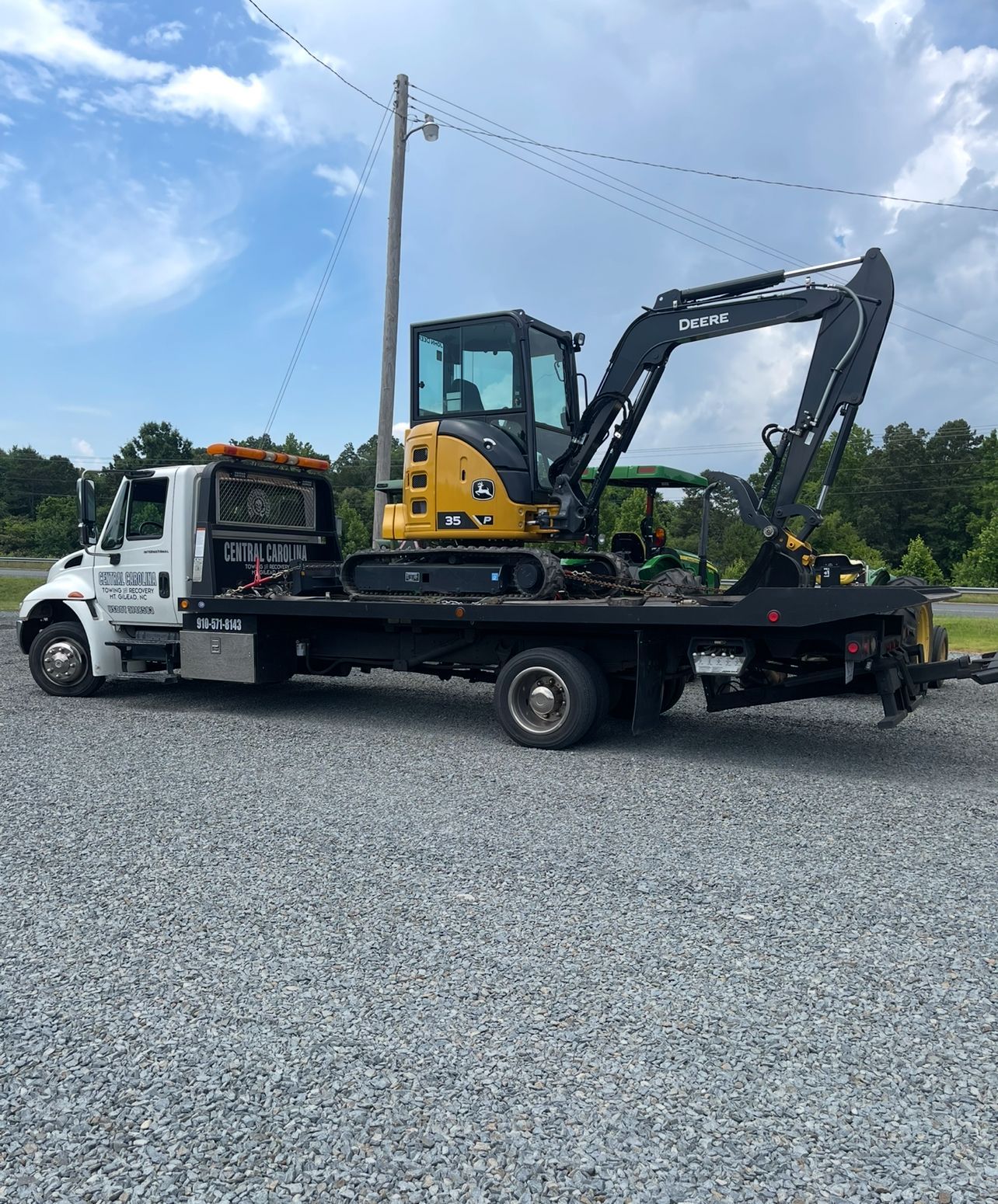 A tow truck is carrying a small excavator on the back of it.