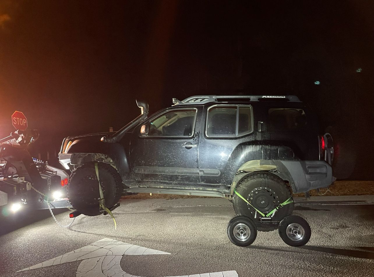 A black suv is being towed by a tow truck at night.