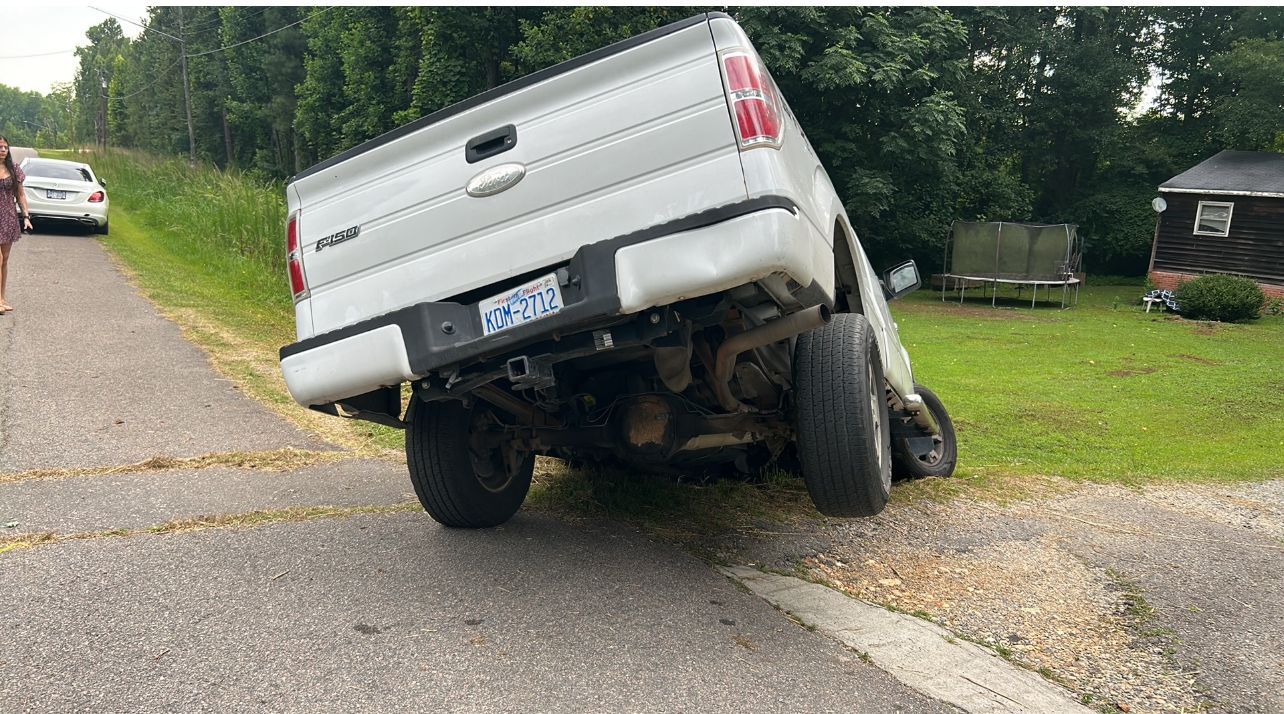A white truck is upside down on the side of the road.