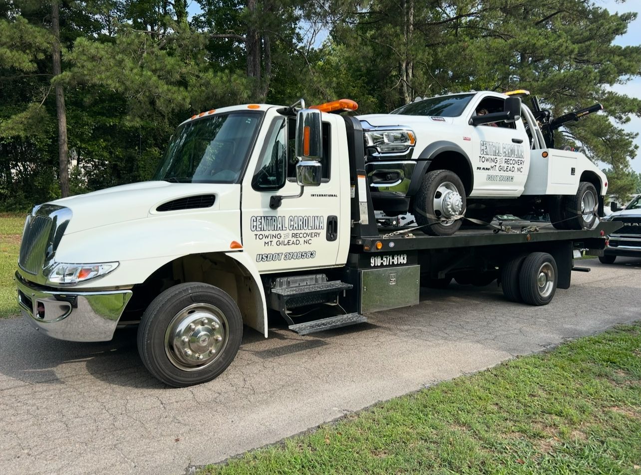 A tow truck with two cars on the back is parked on the side of the road.