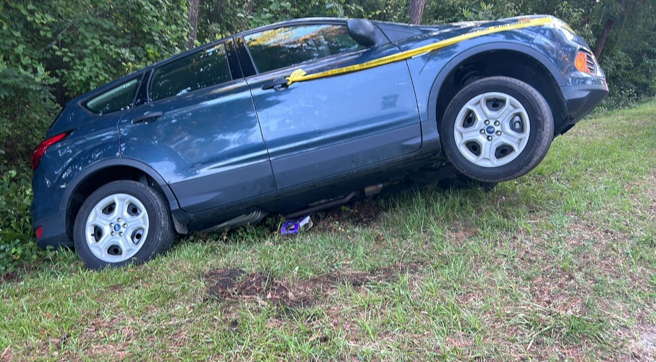 A blue car is sitting on its side in the grass.