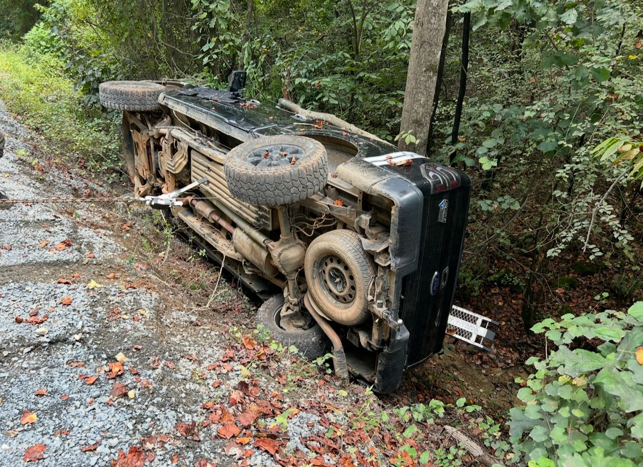A jeep is turned over on its side in the woods.