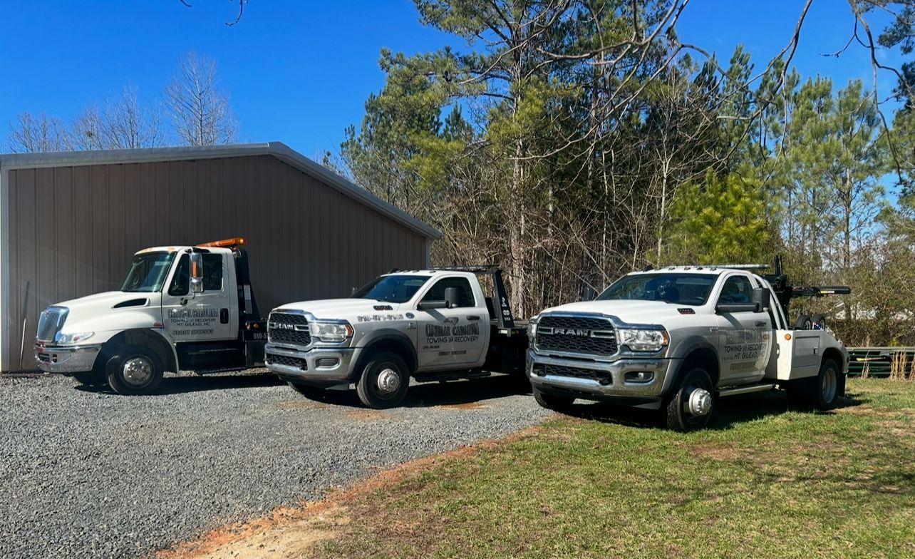 Three tow trucks are parked in front of a garage.
