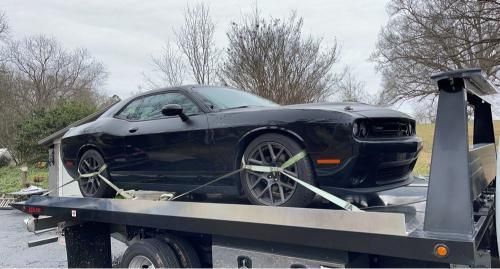 A black dodge challenger is sitting on top of a tow truck.