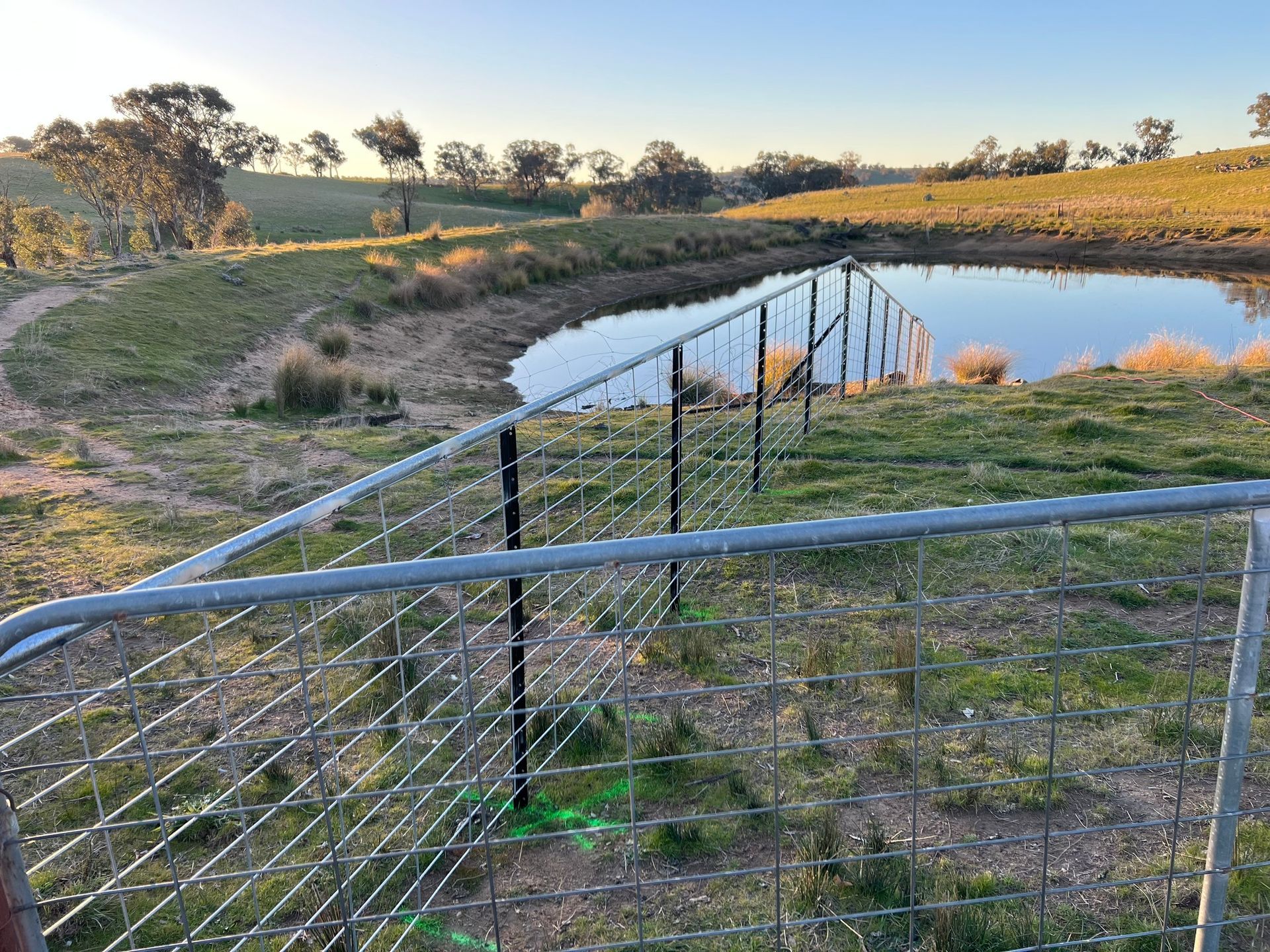 A fence surrounds a small pond in a field.