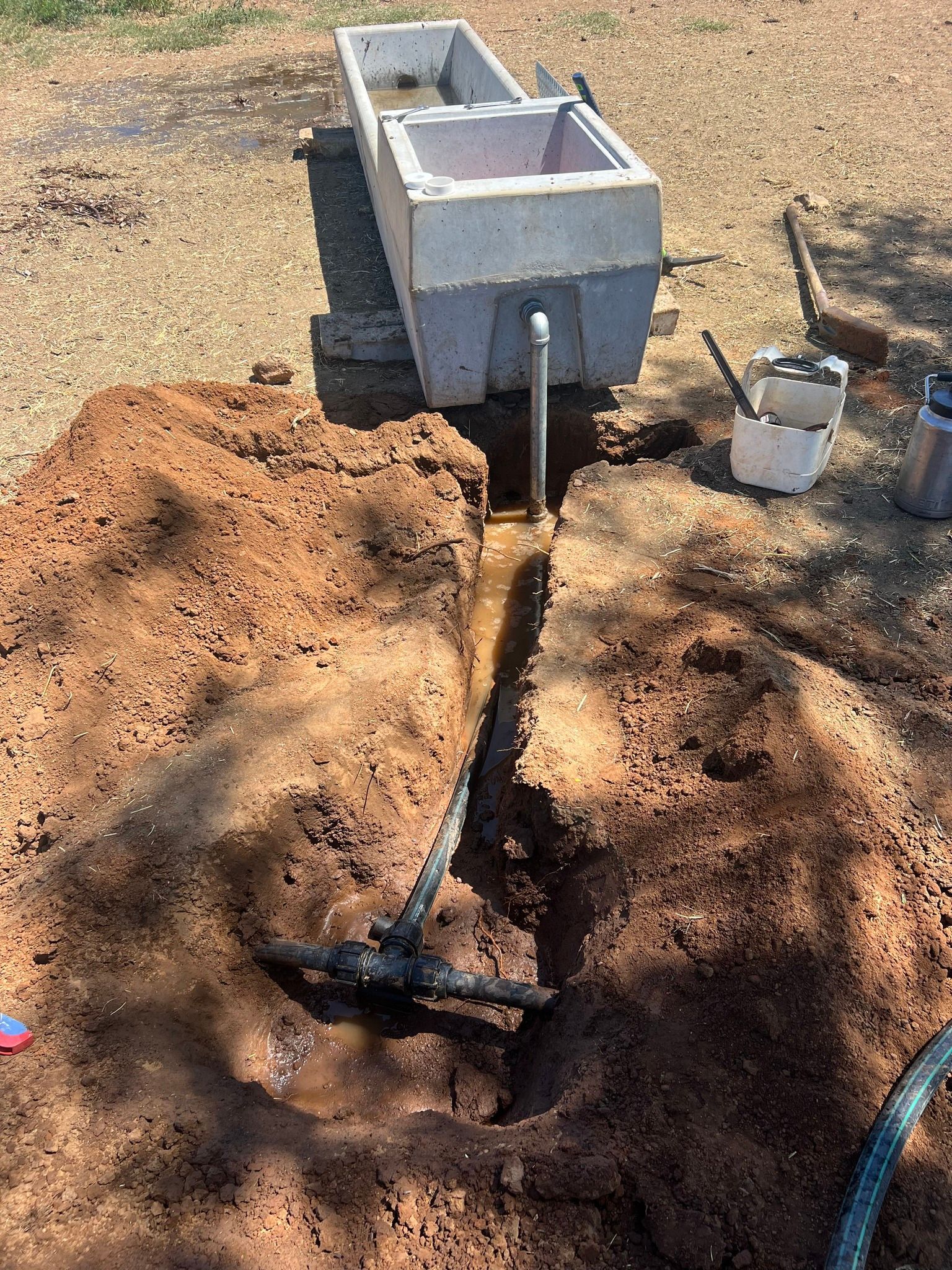 A hose is coming out of a hole in the ground next to a concrete planter.