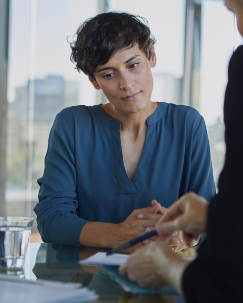 A woman in a blue shirt is sitting at a table talking to another woman