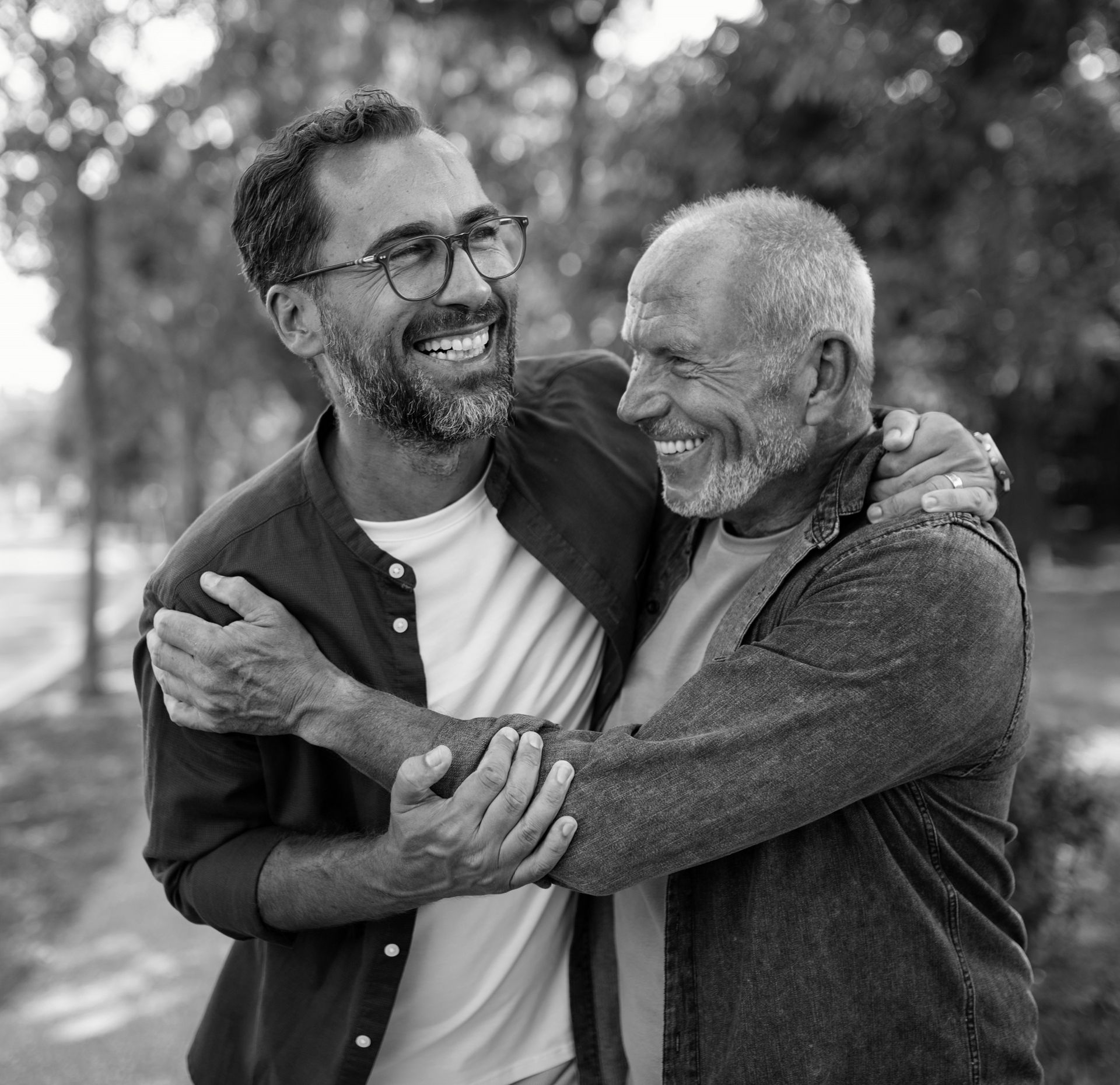 A smiling elderly father and adult son share a hug