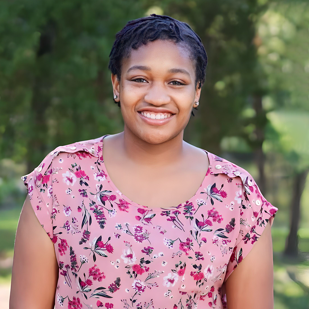 A young woman in a pink floral shirt is smiling for the camera.