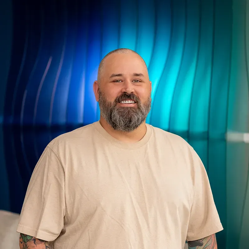 Smiling bearded man in a beige shirt against a blue and teal abstract background