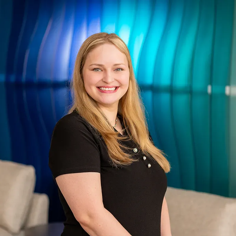 Smiling woman in a black shirt standing in a modern blue-lit interior