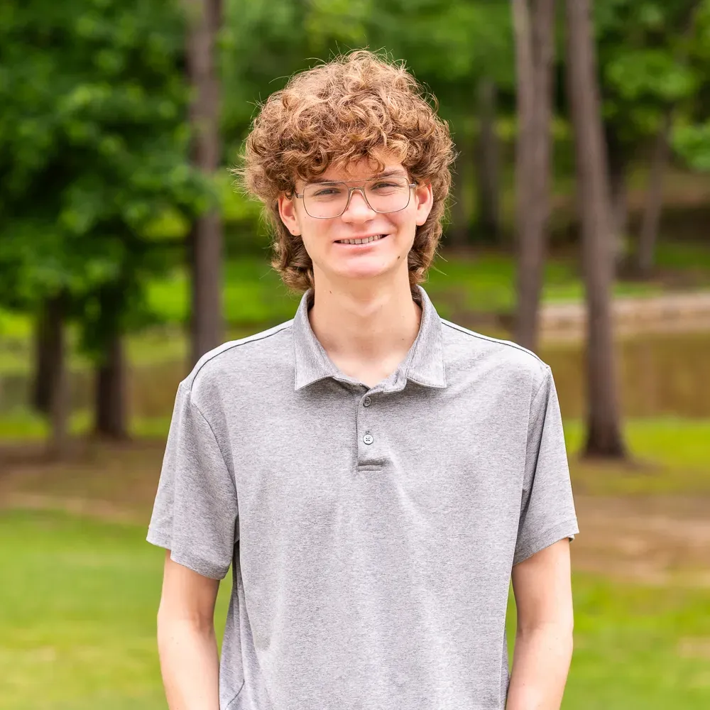 Person with curly hair and glasses standing outdoors