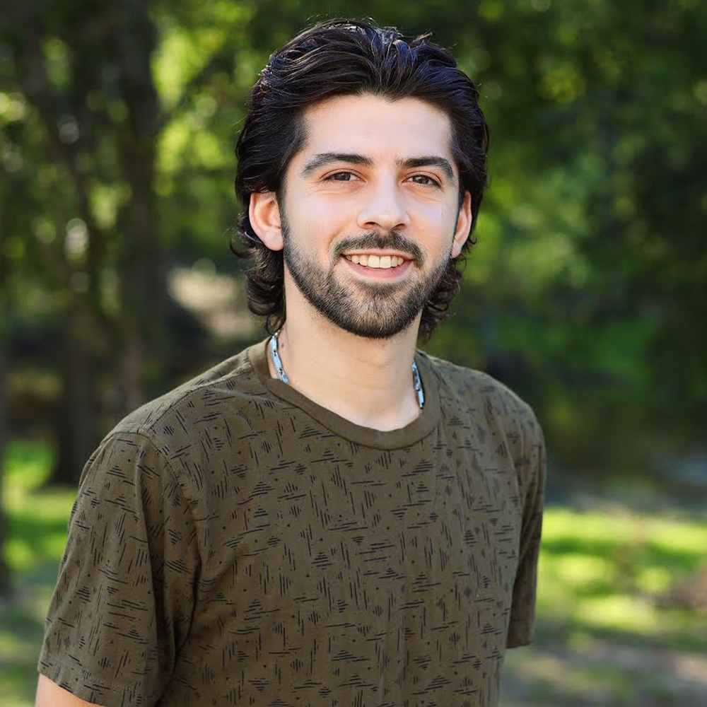 A young man with a beard is wearing a green shirt and smiling for the camera.