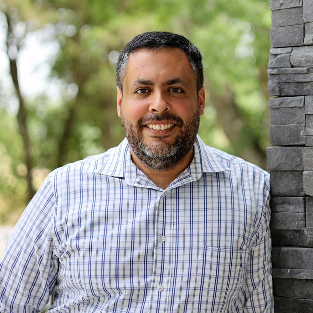 A man with a beard is leaning against a stone wall and smiling.
