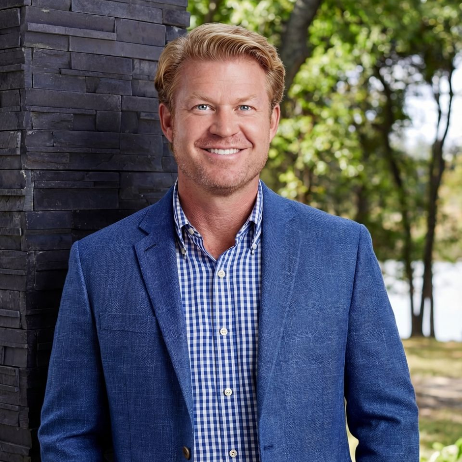 A man in a green sweater is standing with his arms crossed and smiling.