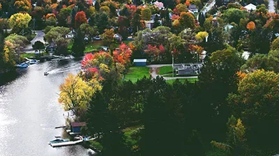 An aerial view of a river winding through a lush forest with colorful autumn trees, featuring several small boats.