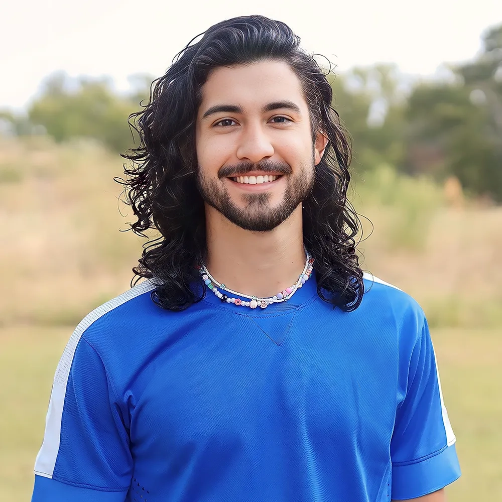A man with long hair and a beard is wearing a blue shirt and smiling.