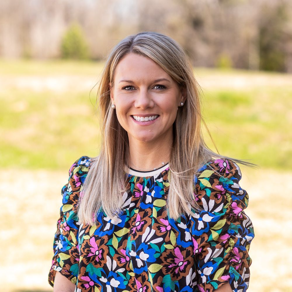 A woman in a colorful floral shirt is smiling for the camera.