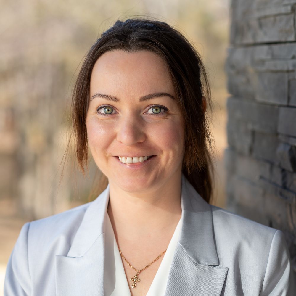 A woman in a grey jacket and white shirt is smiling for the camera.