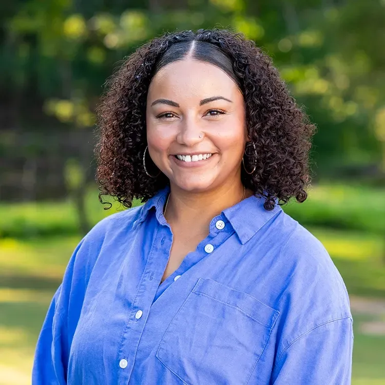 A woman with curly hair is wearing a blue shirt and smiling for the camera.