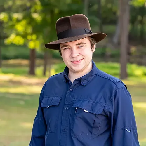 A young man wearing a hat and a blue shirt is standing in a park.