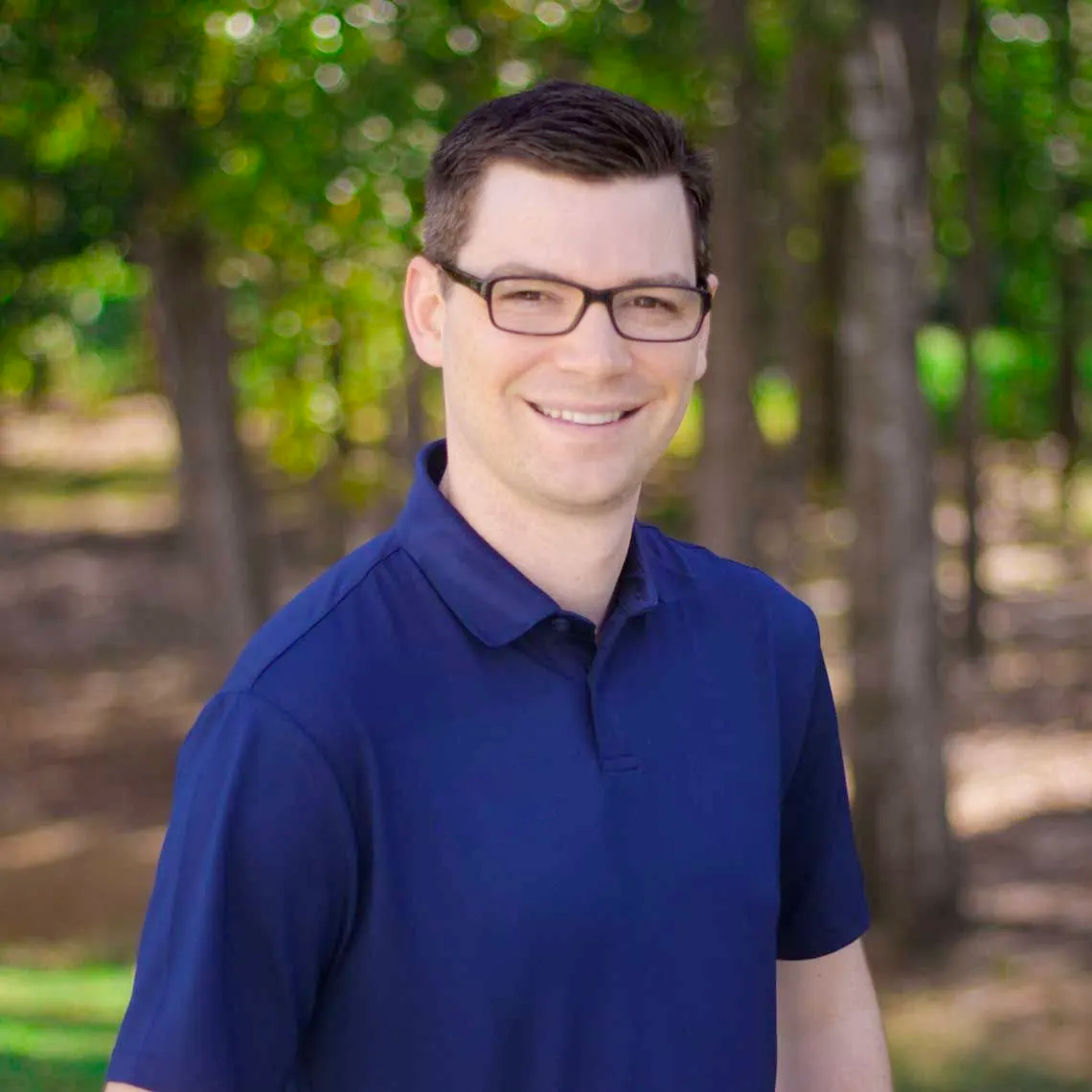 A man wearing glasses and a blue shirt is smiling for the camera.