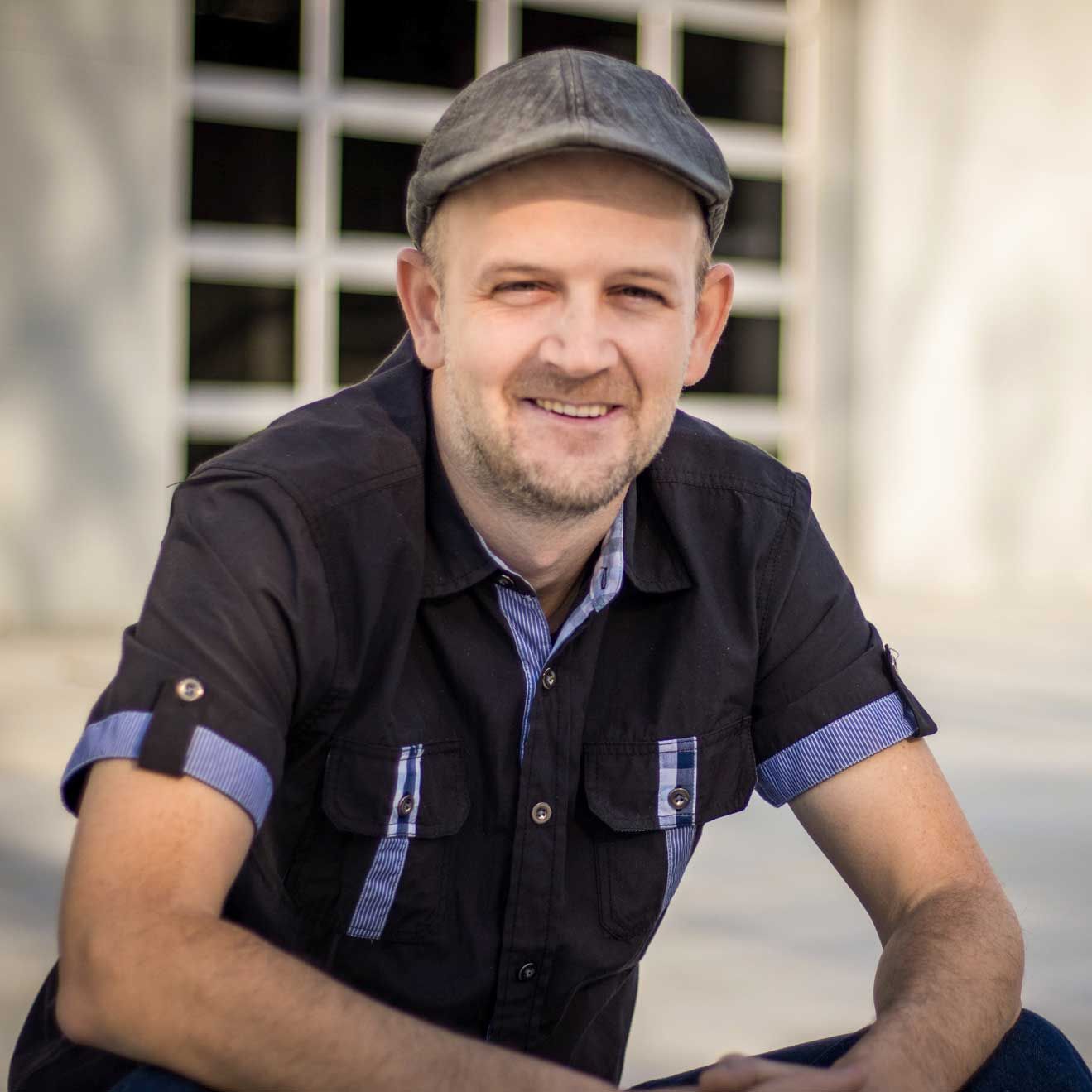 A man wearing a hat and a black shirt smiles for the camera