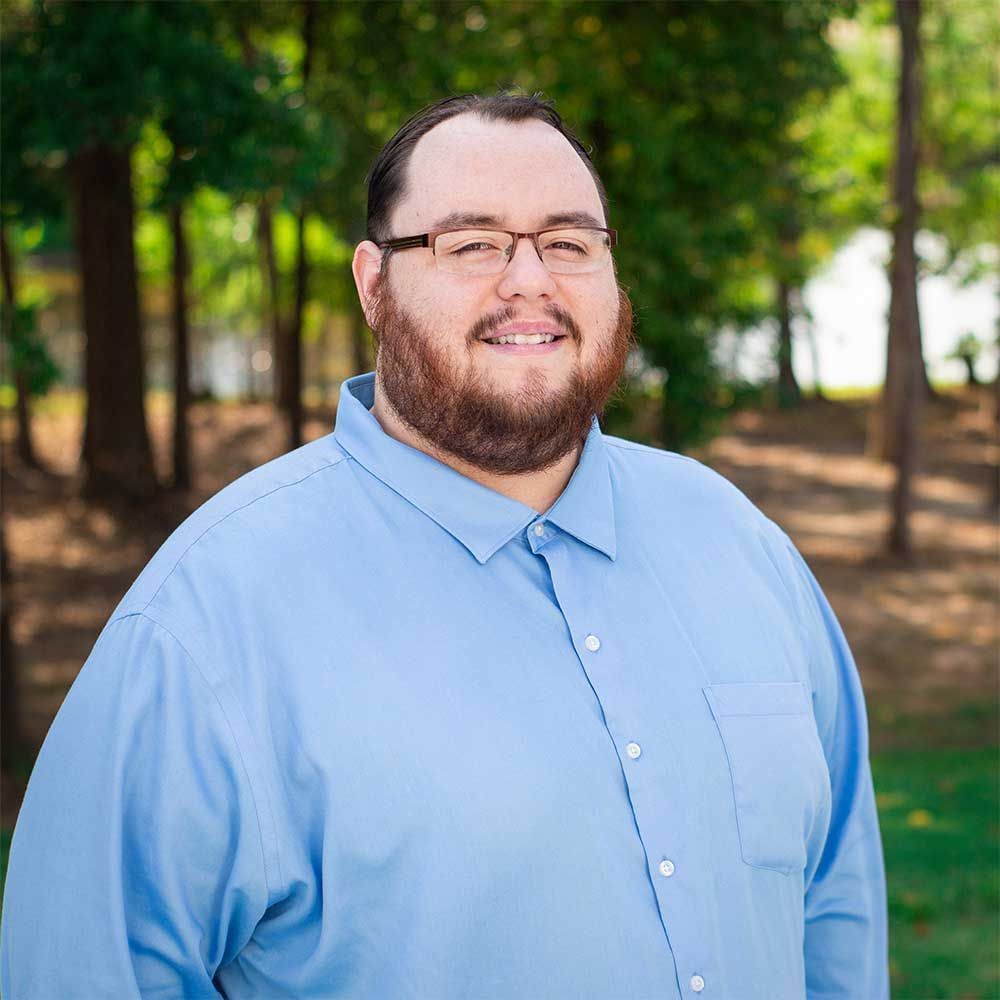 A man with a beard and glasses is wearing a blue shirt and smiling for the camera.