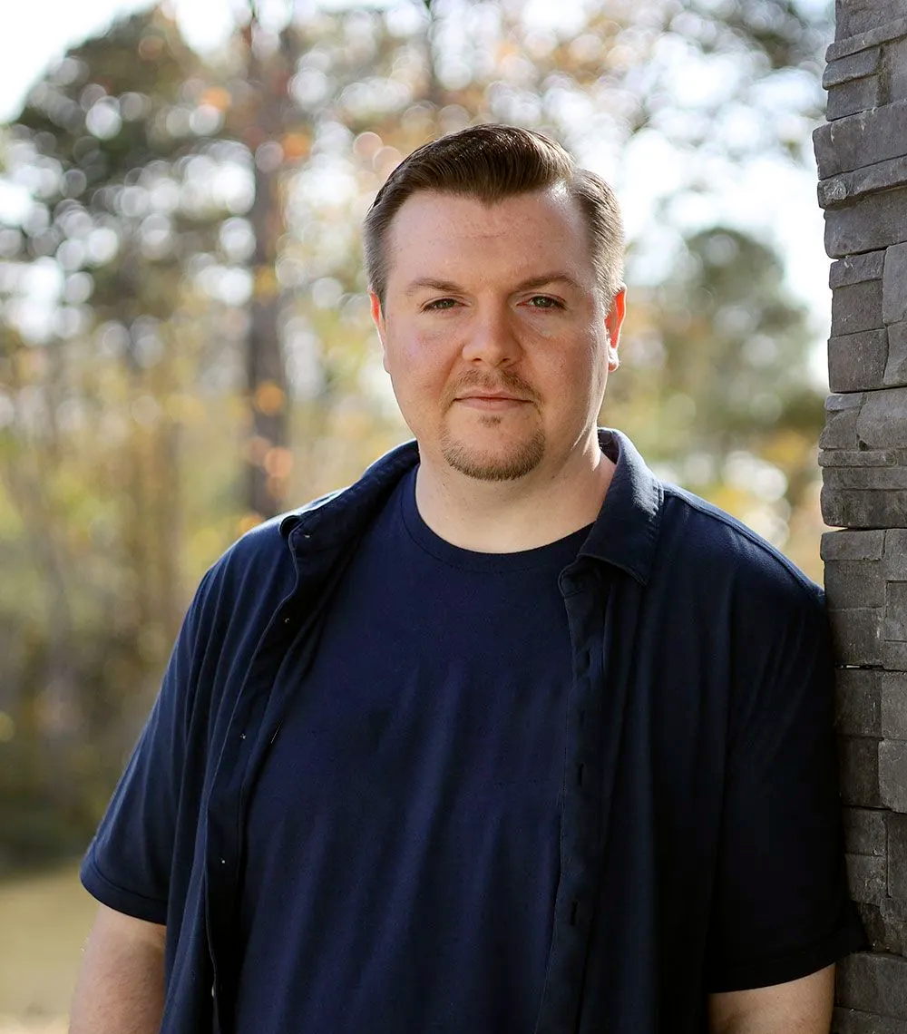 A man in a blue shirt is leaning against a stone wall.