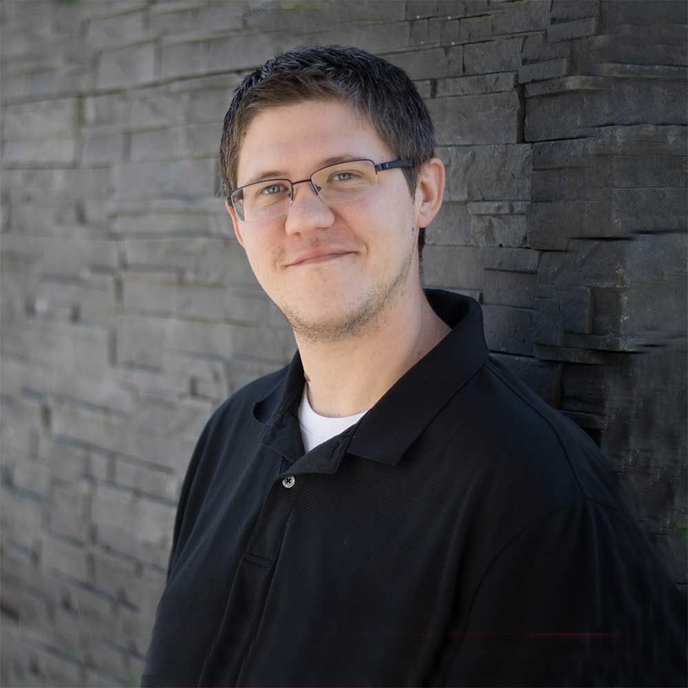 A man wearing glasses and a black shirt is standing in front of a brick wall