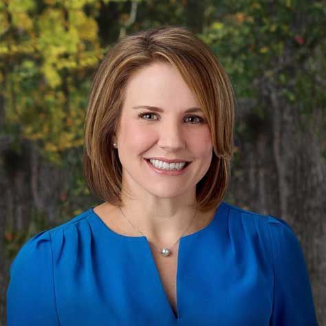 A woman in a blue shirt and necklace is smiling for the camera.