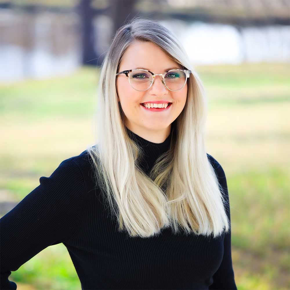 A woman wearing glasses and a black sweater is smiling for the camera.