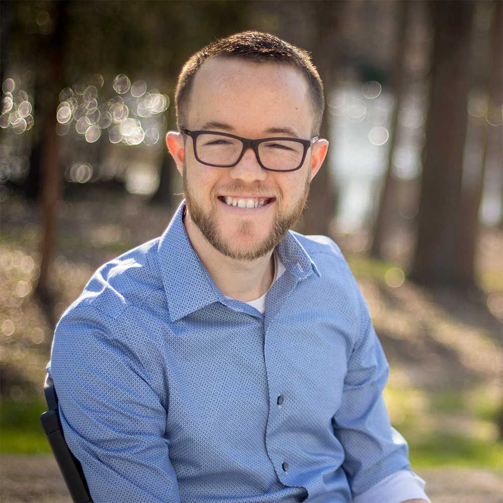 A man wearing glasses and a blue shirt is smiling for the camera.