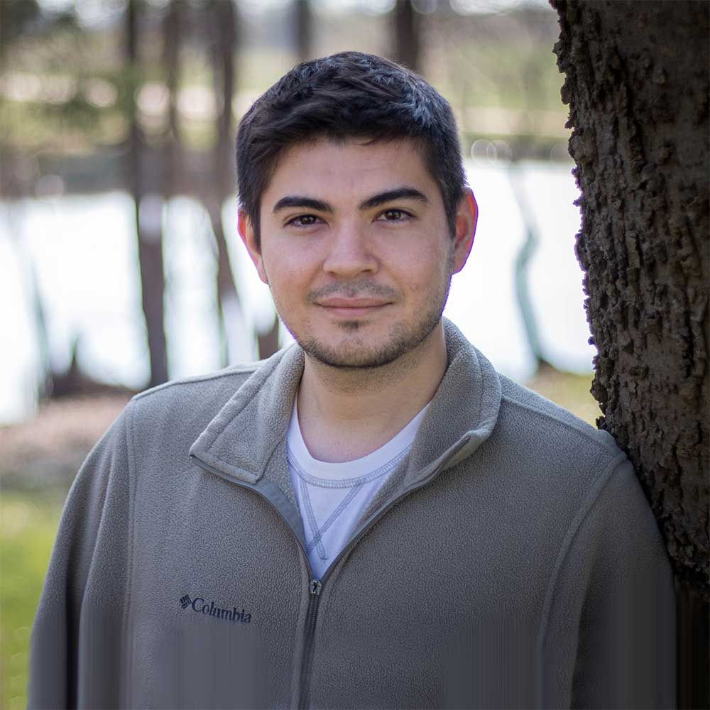 A man in a columbia jacket is leaning against a tree.