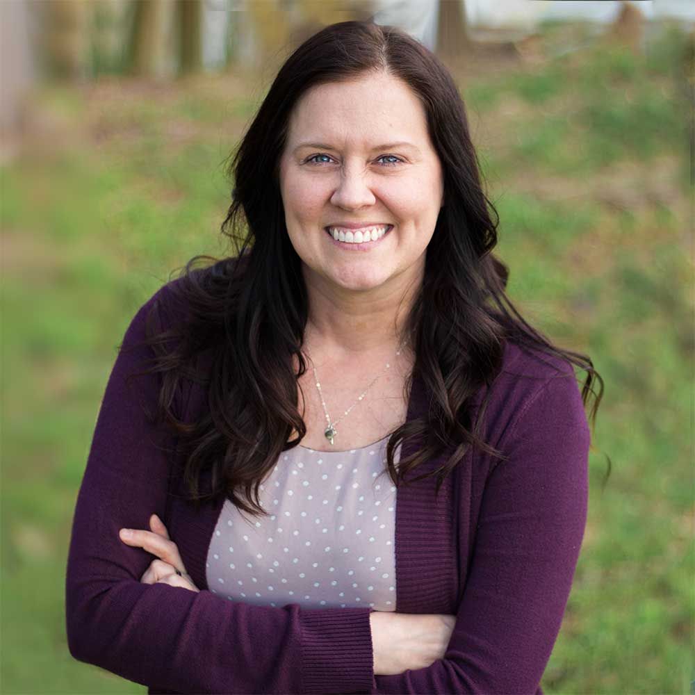 A woman in a purple sweater is smiling with her arms crossed.