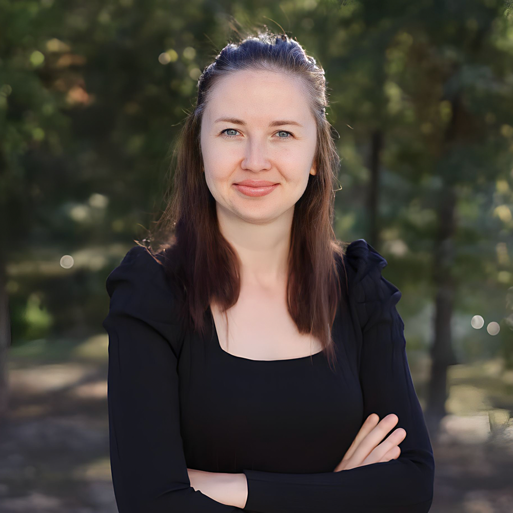 A woman in a black shirt is standing with her arms crossed and smiling.