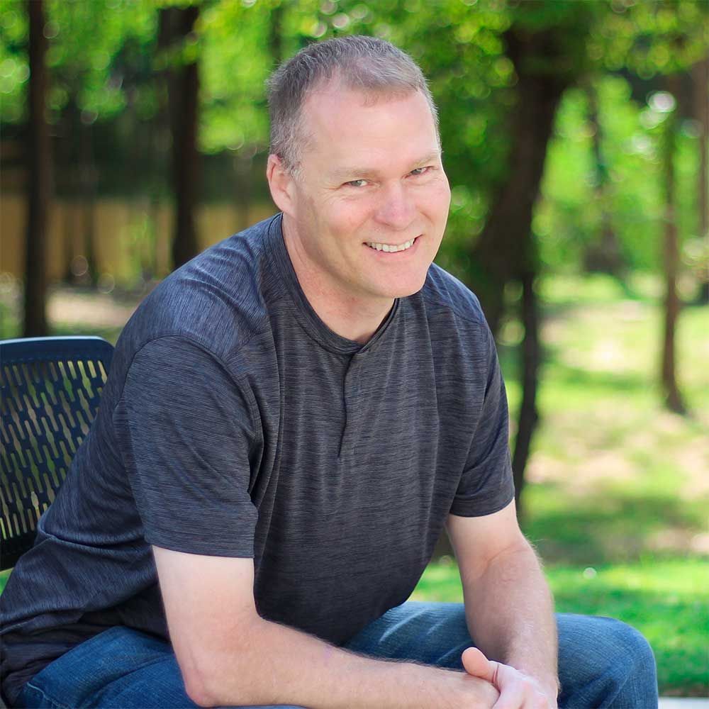 A man is sitting on a bench in a park and smiling.