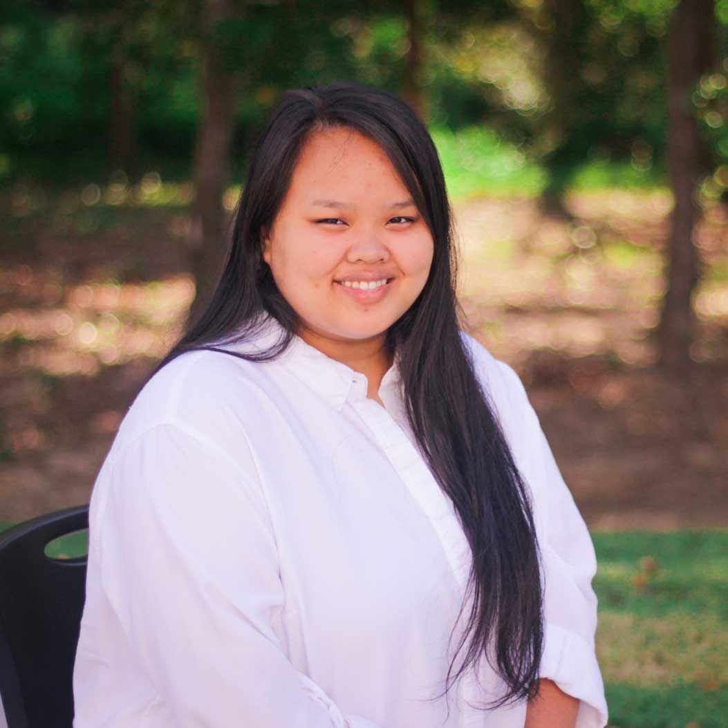A woman in a white shirt is sitting in a chair and smiling for the camera.