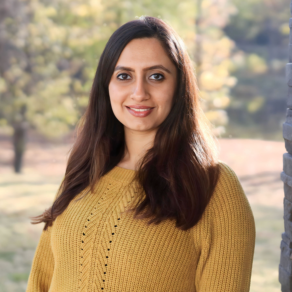 The woman is wearing a yellow sweater and smiling for the camera.