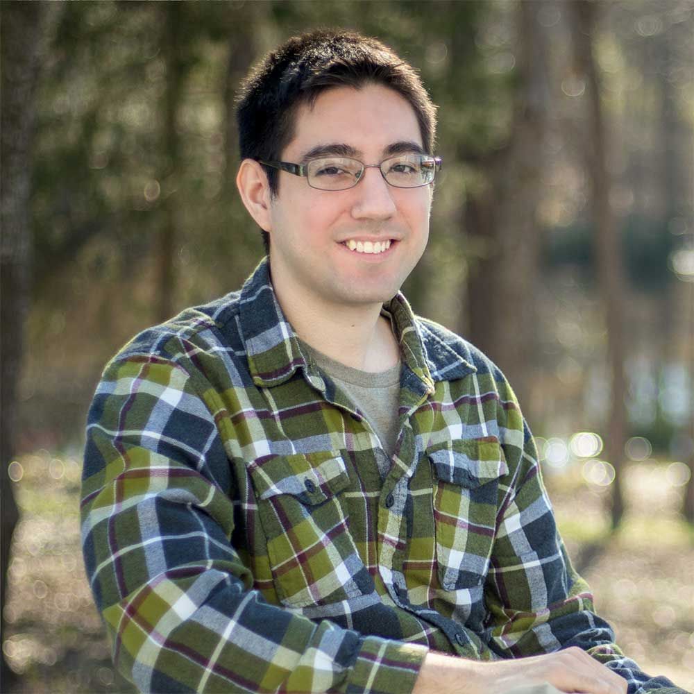 A man wearing glasses and a plaid shirt is smiling for the camera.