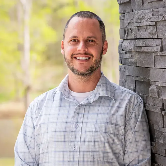 A man with a beard is leaning against a brick wall and smiling.